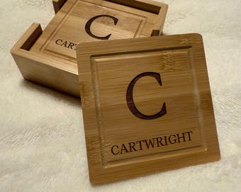 Puede incluir: Un juego de posavasos de bambú con un soporte. Cada posavasos cuadrado tiene un borde empotrado, la letra "C" y el nombre "CARTWRIGHT". El soporte tiene la palabra "CAR" visible.