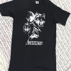 Könnte beinhalten: Schwarzes T-Shirt mit einem weißen Motiv von vier Wölfen und einem Vollmond. Das Wort "BIESZCZADY" ist weiß gedruckt. Das T-Shirt ist aus weichem Material. Klassischer Rundhalsausschnitt.
