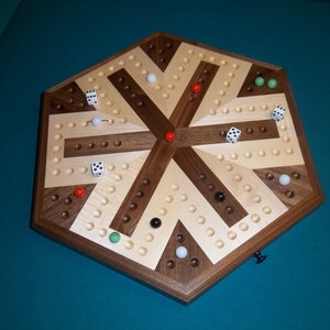 May include: A wooden board game with a hexagonal shape. The game board features a pattern of light and dark wood segments, with small holes and colored marbles. Dice are scattered across the board.