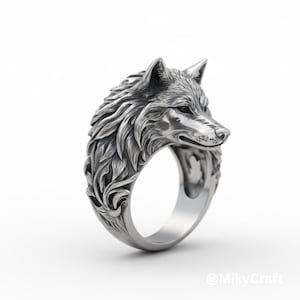 Puede incluir: Un anillo plateado con un diseño detallado de cabeza de lobo. La cabeza del lobo está esculpida con intrincados detalles de pelaje y rasgos faciales. La banda del anillo tiene un patrón floral decorativo. El anillo está sobre un fondo blanco.