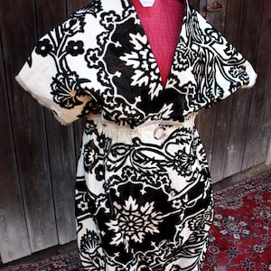 Könnte beinhalten: Ein schwarz-weiß gemustertes Kleid auf einer Schaufensterpuppe. Das Kleid hat ein Blumenmuster und eine betonte Taille mit einer silberfarbenen Schnalle. Das Kleid ist aus weichem, samtigem Material.