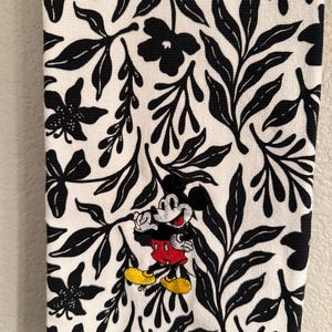 Puede incluir: Toalla de cocina blanca con un patr&oacute;n floral en blanco y negro. Mickey Mouse est&aacute; bordado en el centro de la toalla.