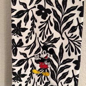 Puede incluir: Toalla de cocina blanca con un patr&oacute;n floral en blanco y negro. Mickey Mouse est&aacute; bordado en el centro de la toalla.
