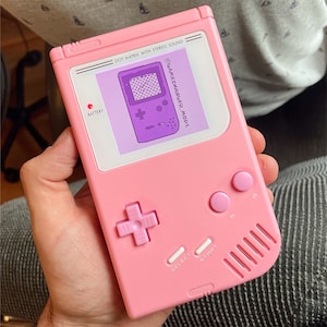 May include: A pink handheld game console with a pixelated game screen, a cross-shaped button, and the text "DOT MATRIX WITH STEREO SOUND" and "@GAMECHANGER_MODS".
