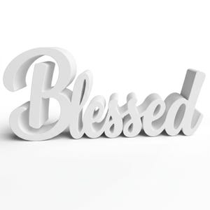Puede incluir: Un letrero blanco tridimensional que deletrea la palabra "Blessed" en cursiva. El letrero est&aacute; hecho de un material s&oacute;lido y est&aacute; sobre un fondo blanco. Las letras est&aacute;n claramente definidas.