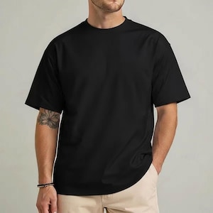 Op de afbeelding: Een effen zwart T-shirt met korte mouwen en een ronde hals. Het shirt is gemaakt van een zacht materiaal en heeft een losse pasvorm. Het model draagt een beige broek.