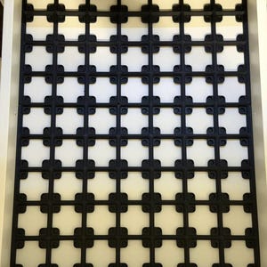 May include: Black grid-patterned drawer liner with a repeating square design. The liner is made of a flexible material and is set inside a white drawer. The design creates a decorative and functional storage solution.