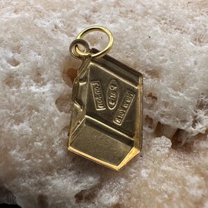 May include: Gold charm shaped like a chocolate bar with the words "Nestle" and "Crunch" on it.