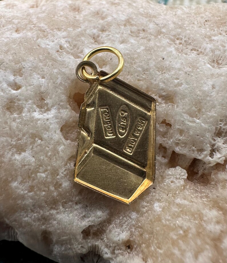 May include: Gold charm shaped like a chocolate bar with the words "Nestle" and "Crunch" on it.