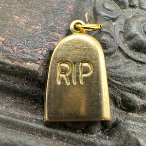 May include: Gold-colored metal charm shaped like a tombstone with the word "RIP" engraved on the front.