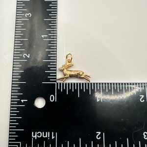 K&ouml;nnte beinhalten: Ein goldfarbener Hirsch-Anh&auml;nger, etwa 2,5 cm lang, mit einem detaillierten Design und einer &Ouml;se zum Anbringen an einer Kette oder einem Armband.