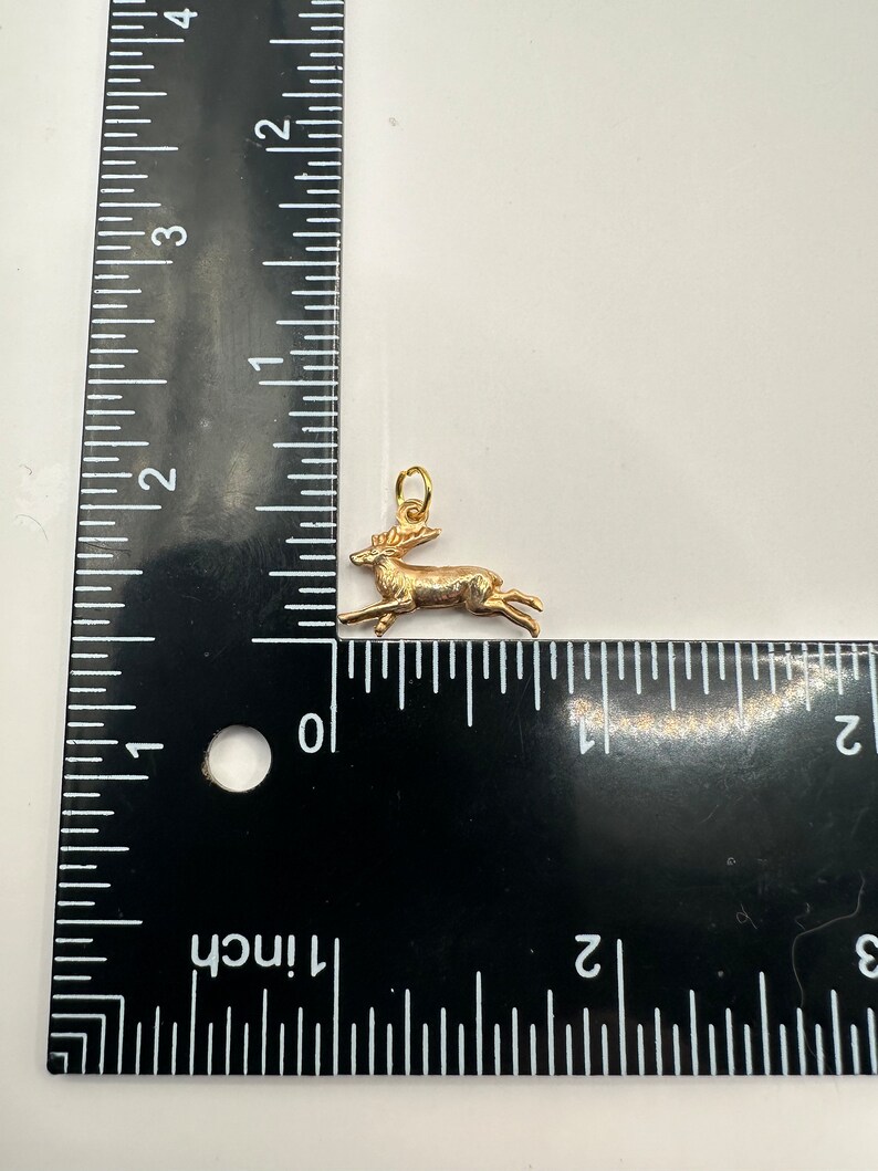 K&ouml;nnte beinhalten: Ein goldfarbener Hirsch-Anh&auml;nger, etwa 2,5 cm lang, mit einem detaillierten Design und einer &Ouml;se zum Anbringen an einer Kette oder einem Armband.