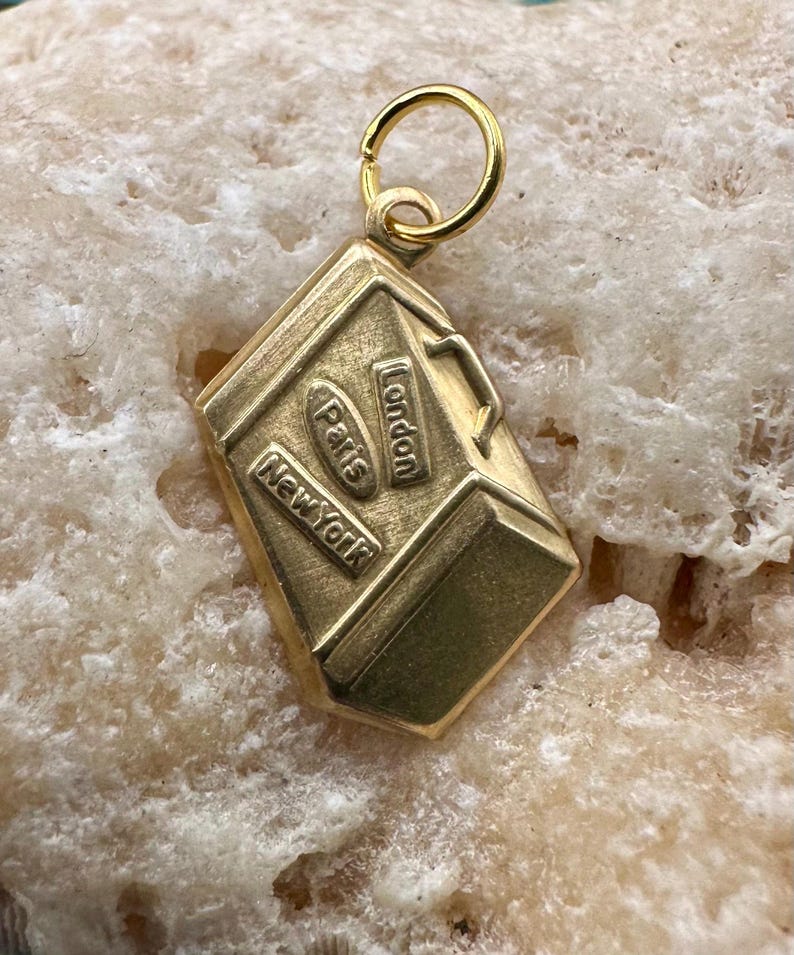May include: Gold-toned charm shaped like a suitcase with the words "London", "Paris", and "New York" on it.