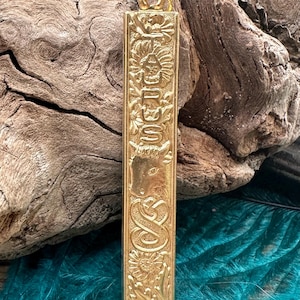 May include: Gold-colored pendant with the word "Taurus" engraved in a decorative font. The pendant is surrounded by floral designs and a bull's head.