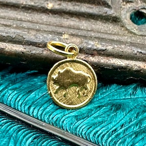 May include: Gold-colored pendant charm featuring a detailed silhouette of a wild boar. The charm is round and has a textured surface.