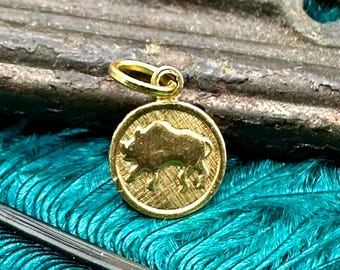 May include: Gold-coloured pendant charm featuring a detailed silhouette of a wild boar. The charm is round and has a textured surface.