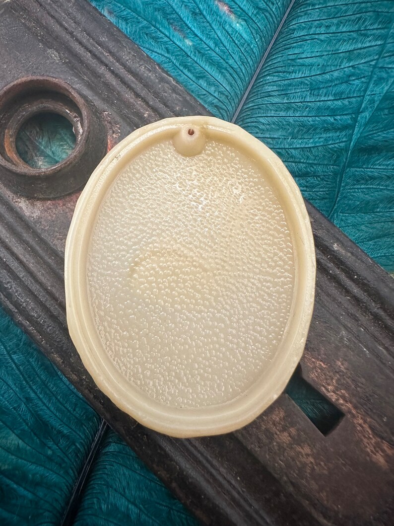 May include: A white oval ceramic incense burner with a small hole in the center. The burner has a textured surface and is sitting on a wooden surface.