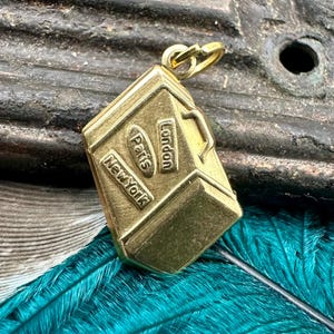 May include: Gold-toned metal charm shaped like a suitcase with the words "London", "Paris", and "New York" on it.
