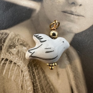 May include: A white ceramic dove charm with gold accents. The dove has a simple, elegant design and is perfect for adding a touch of whimsy to any jewelry piece.