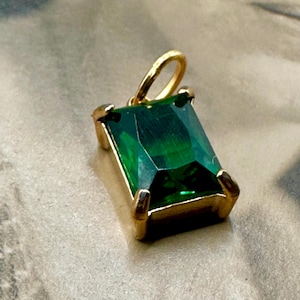 May include: A gold pendant with a large, emerald green gemstone set in a rectangular frame.