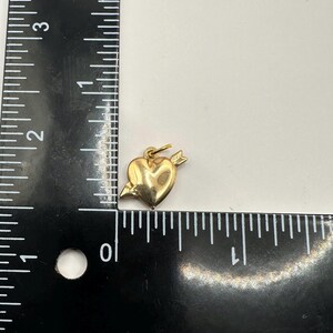 May include: A gold-coloured heart charm with an arrow through it. The charm is approximately 2.5 cm in length.