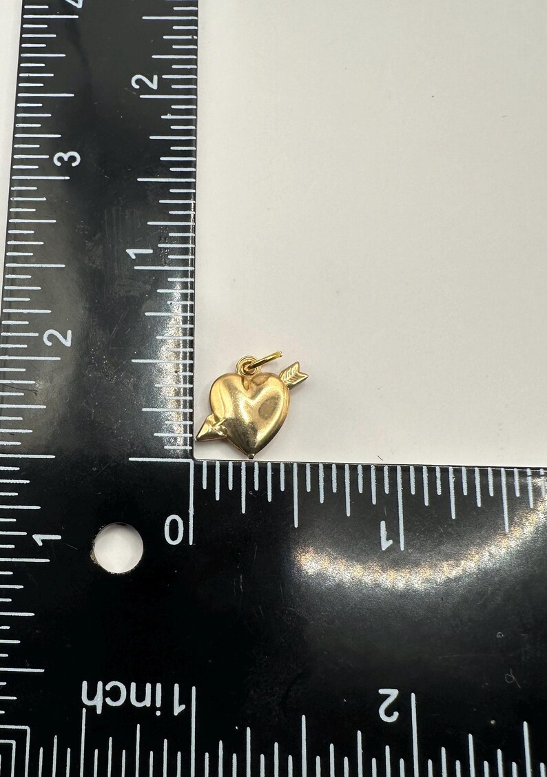 May include: A gold-coloured heart charm with an arrow through it. The charm is approximately 2.5 cm in length.