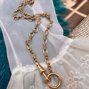 Puede incluir: Un collar de cadena de oro con un cierre grande y redondo. La cadena está hecha de eslabones ovalados y redondos unidos.