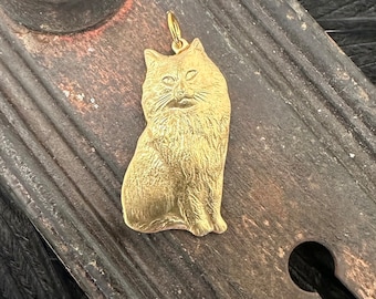 May include: A gold-colored metal pendant shaped like a sitting cat. The cat has a detailed, textured surface and a realistic expression.