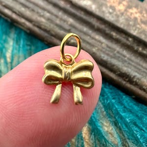 May include: A small gold charm in the shape of a bow. The charm has a loop at the top for attaching to a necklace or bracelet.