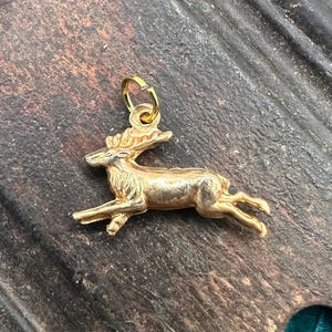 K&ouml;nnte beinhalten: Ein goldfarbener Hirsch-Anh&auml;nger. Der Hirsch ist in einer laufenden Pose dargestellt, mit dem Kopf zur Seite gedreht. Der Anh&auml;nger hat eine Schlaufe oben zum Anbringen an einer Halskette oder einem Armband.