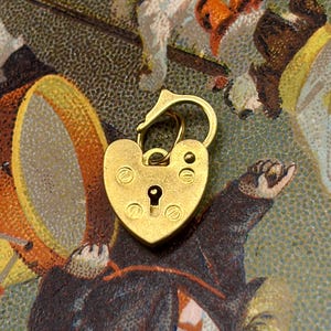 May include: A heart-shaped brass padlock with a keyhole and a curved handle. The padlock is gold-colored and has a vintage aesthetic. The background features a colorful illustration with figures and shapes.