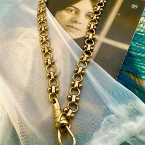 May include: A gold chain necklace with a large, round, decorative clasp. The chain is made of linked circles with small, round beads between each link.