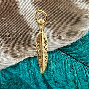 May include: A gold-colored feather charm with a loop at the top for attaching to a necklace or bracelet.
