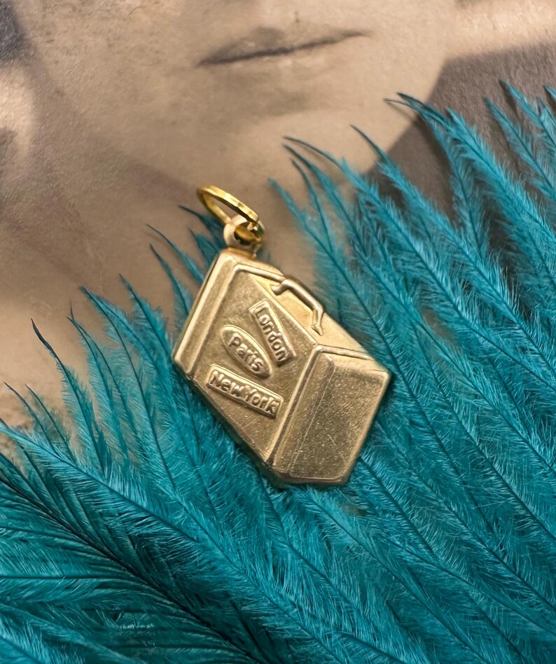 May include: Gold-toned luggage charm with the words "London", "Paris", and "New York" on it.
