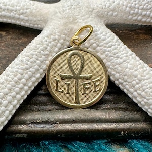 May include: A gold-colored pendant with the word "LIFE" and an ankh symbol. The pendant is round with a textured background. The pendant is on a white starfish.