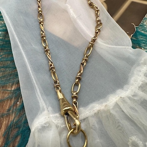 May include: A gold chain necklace with a twisted design and a clasp with a ring. The chain is on a white fabric background.