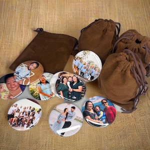Könnte beinhalten: Eine Sammlung personalisierter Fotoknöpfe mit verschiedenen Familienporträts und Gruppenfotos. Die Knöpfe sind rund und glänzend, mit Bildern von Menschen. Sie werden von mehreren kleinen, braunen Kordelzugbeuteln begleitet, die alle auf einer strukturierten, hellbraunen Oberfläche angeordnet sind.
