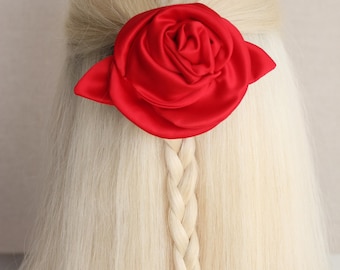 Op de afbeelding: Een felrode satijnen rozenhaarclip siert blond haar, gevlochten in een vlecht. Het haaraccessoire is een grote, opvallende bloem die een vleugje elegantie toevoegt. Deze haarclip is perfect voor speciale gelegenheden of dagelijks gebruik.