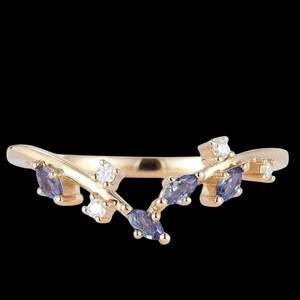Könnte beinhalten: Ein goldfarbener Ring mit einem zarten, von der Natur inspirierten Design. Der Ring hat kleine, marquiseförmige blaue Edelsteine und runde, klare Edelsteine, die wie Blätter und Blüten angeordnet sind. Der Ring ist vor einem schwarzen Hintergrund platziert.
