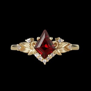 Könnte beinhalten: Ein goldener Ring mit einem rautenförmigen, tiefroten Edelstein als Mittelpunkt. Der Ring hat ein florales Design mit kleinen, klaren Edelsteinen, vor schwarzem Hintergrund.