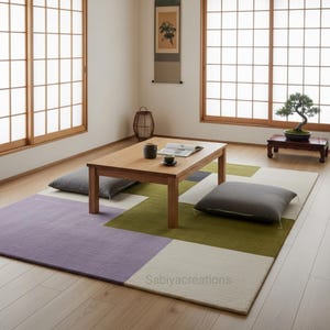 May include: A minimalist Japanese-style living room featuring a low wooden table, floor cushions, and a geometric rug in shades of purple, green, and white. A bonsai tree sits on a small wooden stand, enhancing the serene atmosphere.