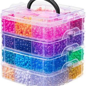 May include: A clear plastic bead organizer with a black handle, filled with various colors of beads. The beads are arranged in separate compartments, showcasing shades of pink, orange, purple, blue, green, and yellow. The organizer is designed for craft supplies.
