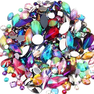 May include: A collection of iridescent rhinestones in various shapes and sizes, including teardrops, ovals, and squares. The gems are in shades of red, blue, green, and purple, with a shimmering, reflective quality. These decorative embellishments are ideal for crafts and jewelry making.