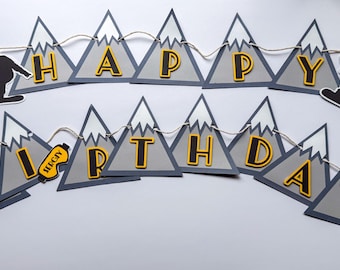 Puede incluir: Una pancarta festiva de "Feliz Cumpleaños" con un tema de snowboard. La pancarta presenta banderines grises en forma de montaña con letras amarillas y negras. Siluetas de snowboarders están unidas a la cuerda.