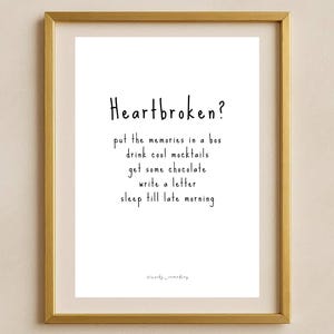 Può includere: Una stampa incorniciata con il testo "Heartbroken?" seguito da suggerimenti in stile manoscritto. La cornice è dorata e lo sfondo è bianco. Il testo include frasi come "drink cool mocktails" e "sleep till late morning."