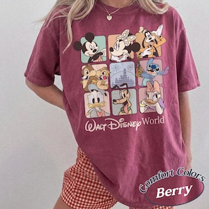 May include: Berry-colored t-shirt featuring a grid of Disney characters including Mickey Mouse, Minnie Mouse, and Goofy. The shirt has the words "Walt Disney World" printed below the grid. The shirt is a Comfort Colors brand.