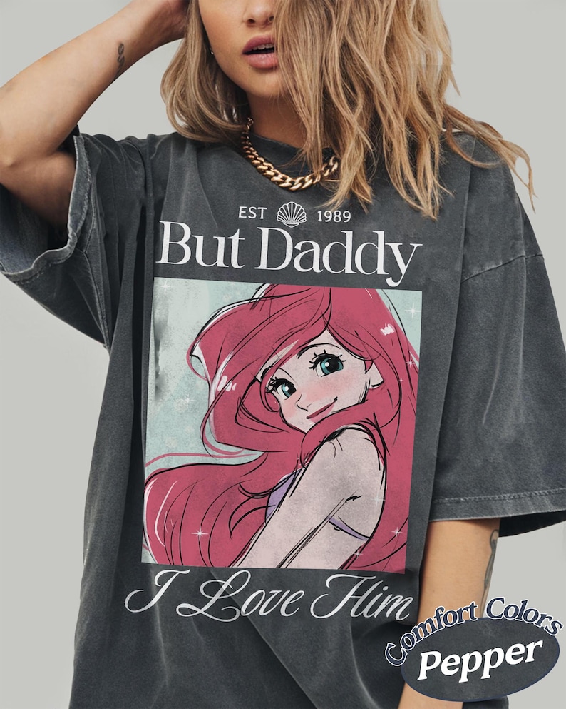 K&ouml;nnte beinhalten: Dunkelgraues T-Shirt mit dem Text "But Daddy I Love Him" und einer Cartoon-Grafik mit roten Haaren und blauen Augen. Das Shirt ist von Comfort Colors.