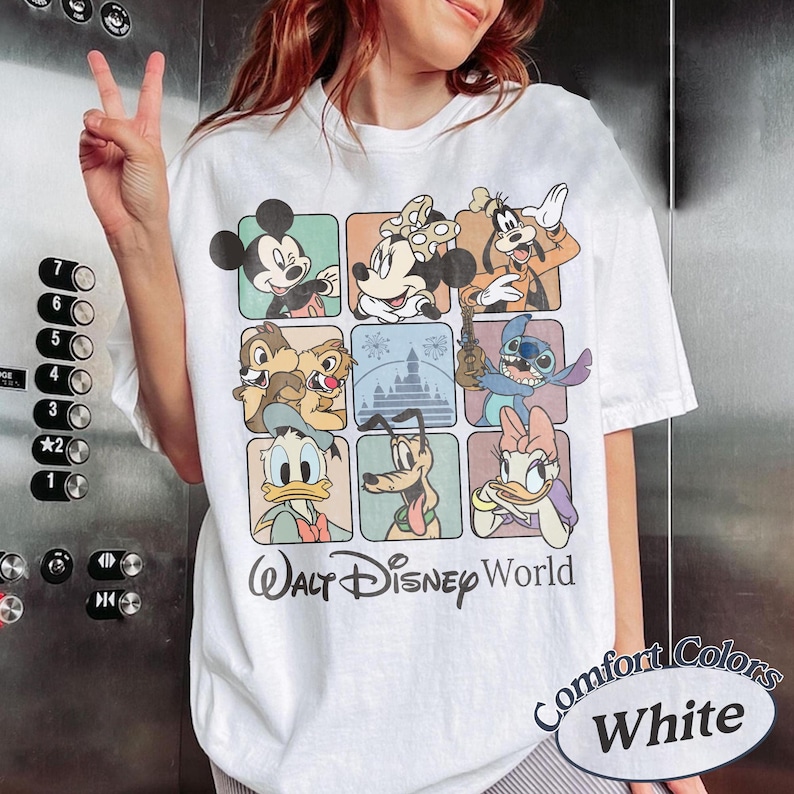 May include: White t-shirt featuring a grid of Disney characters including Mickey Mouse, Minnie Mouse, and Goofy. The shirt has the text "Walt Disney World" and "Comfort Colors White" printed on it. The shirt is a short-sleeved, casual style.