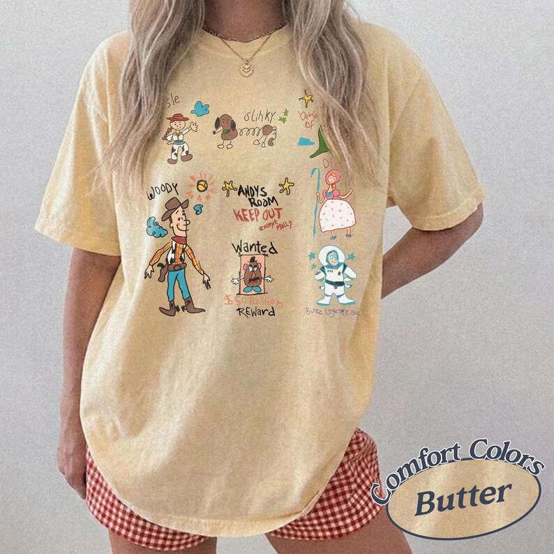Puede incluir: Camiseta de color mantequilla con personajes de dibujos animados y texto. El dise&ntilde;o incluye a Woody, Slinky y Buzz Lightyear, con las palabras "ANDYS ROOM KEEP OUT" y "WANTED REWARD". La camiseta es de la marca Comfort Colors.