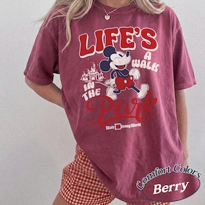 May include: Berry-colored t-shirt featuring Mickey Mouse and the text "LIFE'S A WALK IN THE PARK" with "Walt Disney World" below. The shirt has a vintage look and is made of Comfort Colors material.